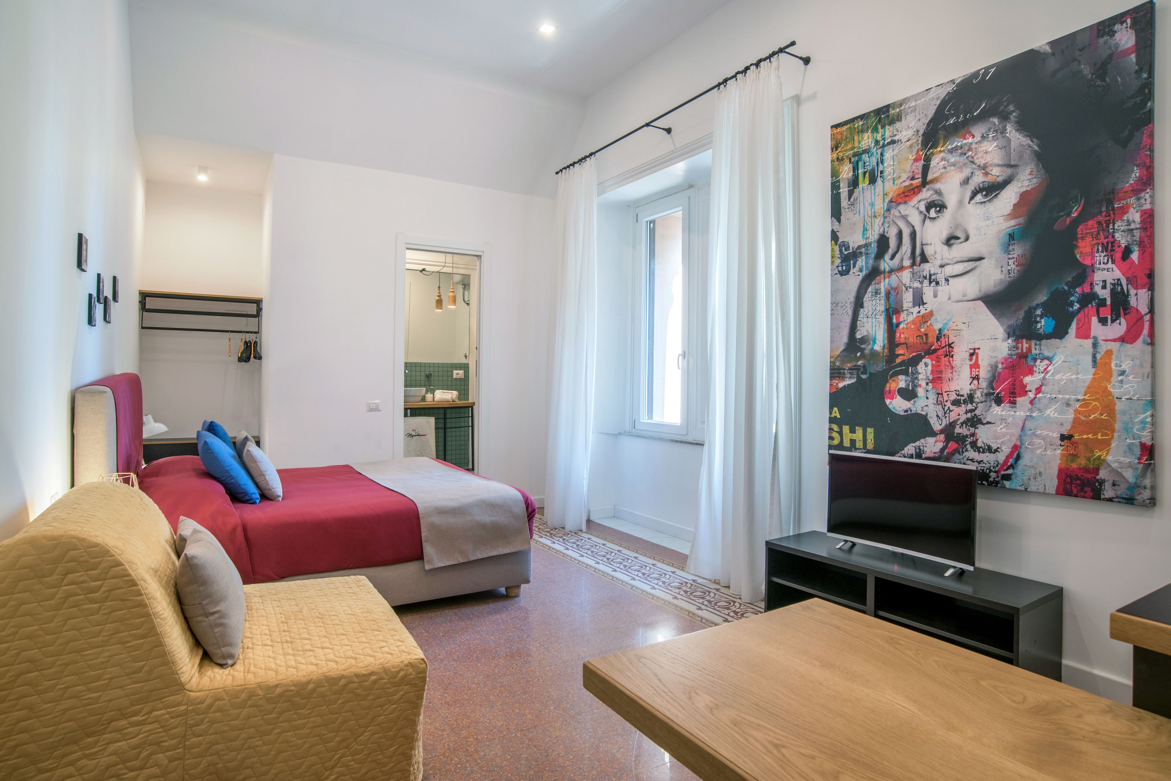 Een moderne hotelkamer met een bed, een bank, een televisie en een groot abstract schilderij.