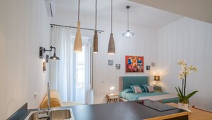 A modern kitchen with a large island, pendant lights, and a view into a bedroom with a bed and a painting on the wall. - Napoliamo Guest House (Naples)