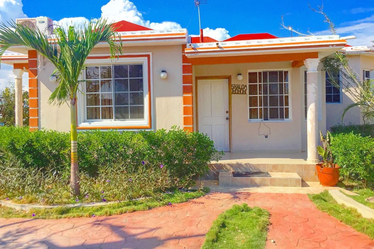 Una casa de dos pisos con techo rojo, paredes exteriores blancas y un porche pequeño en la entrada.