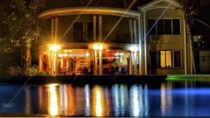 Een gebouw aan het water met een bar, grote ramen en een zwembad.