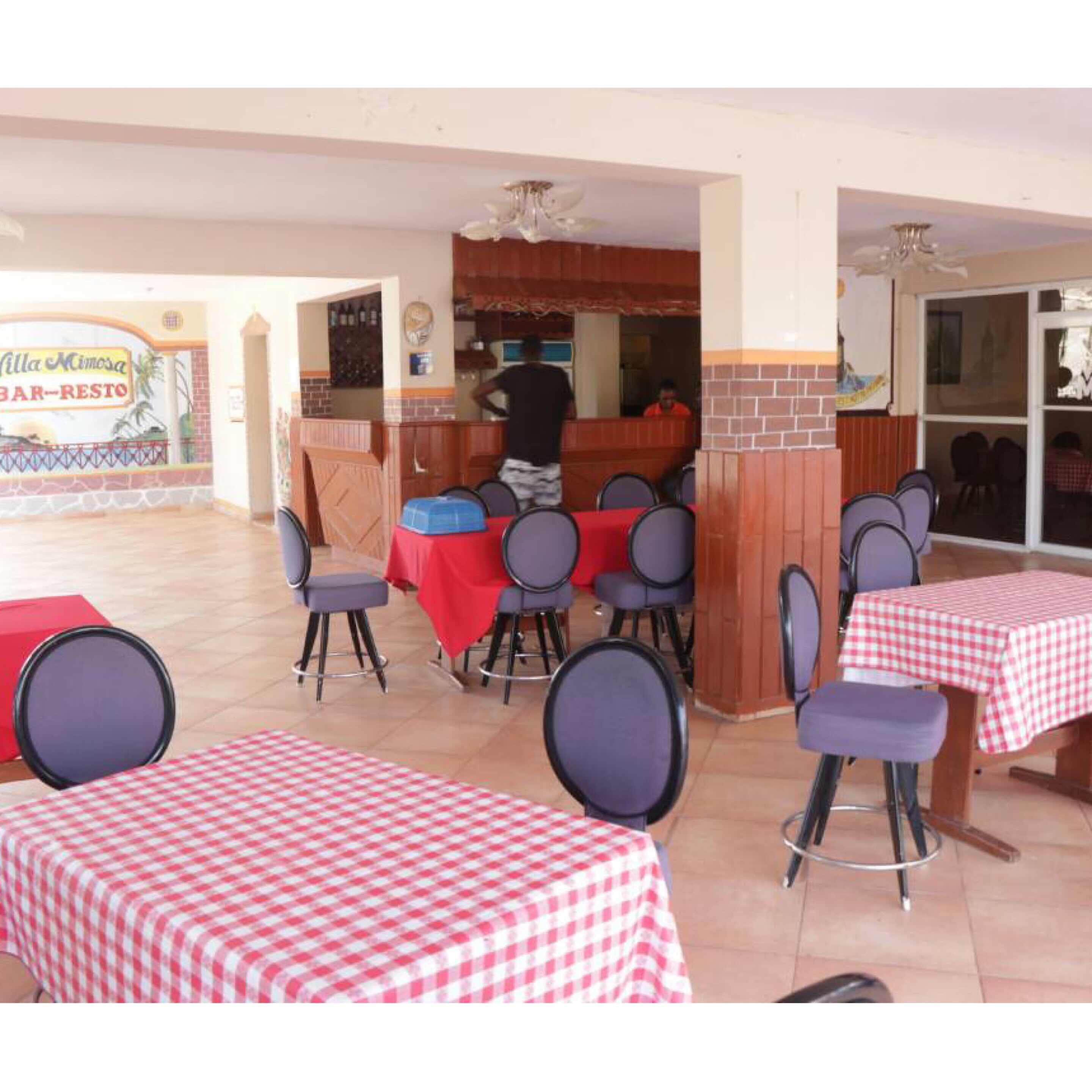 An outdoor dining area with tables covered in red and white checkered tablecloths, surrounded by chairs.