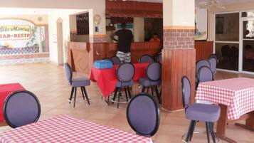 An outdoor dining area with tables covered in red and white checkered tablecloths, surrounded by chairs.