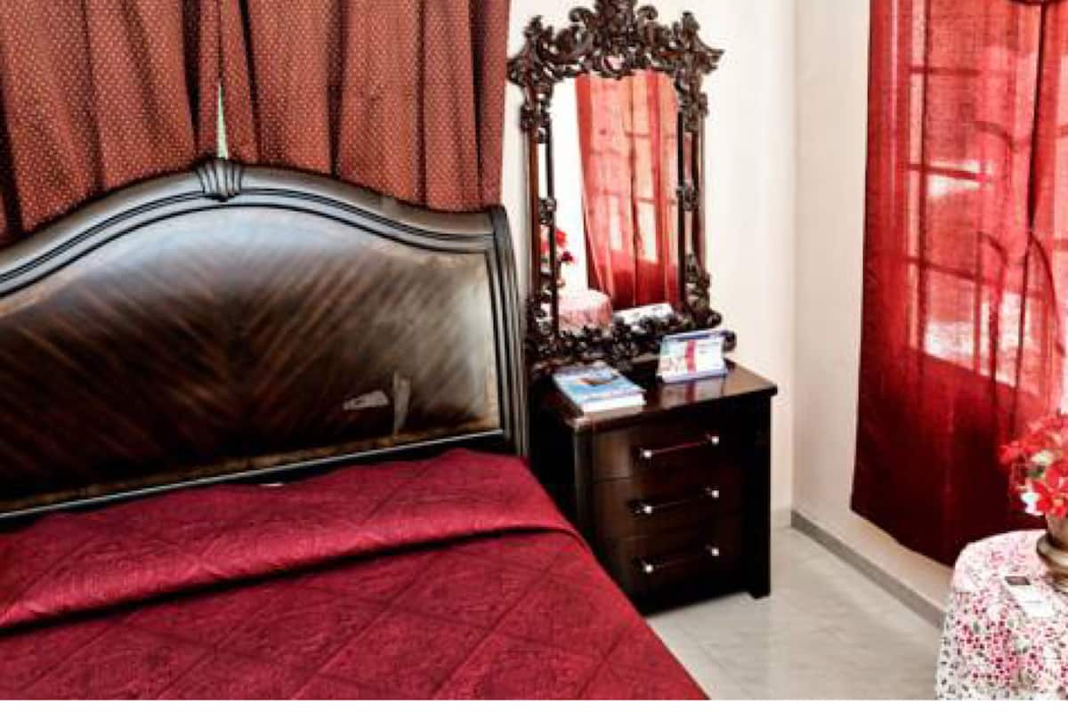 Un dormitorio con una cama, un aparador, un espejo y cortinas rojas.