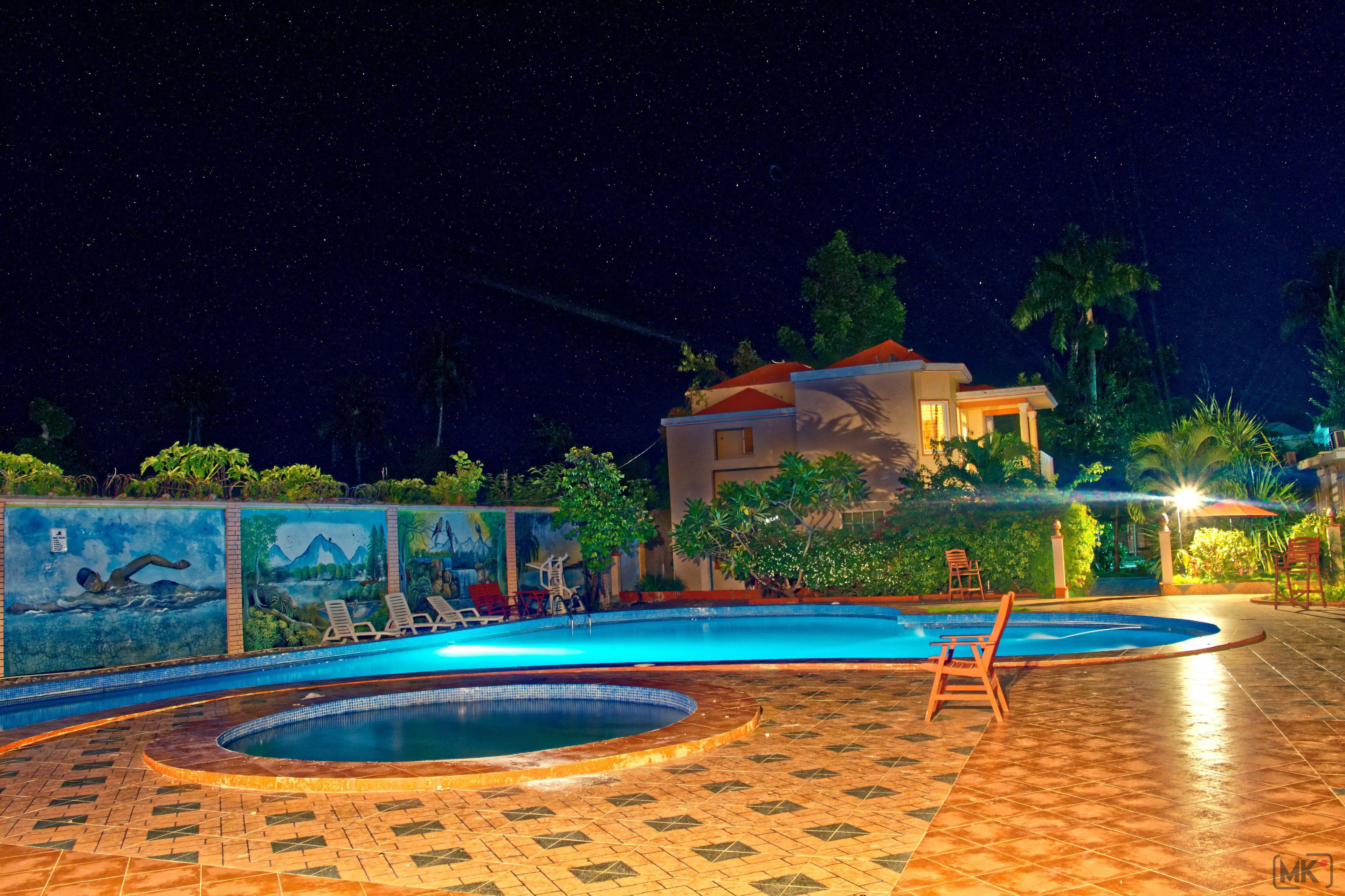 A swimming pool with a tiled deck, lounge chairs, and a mural on the wall.