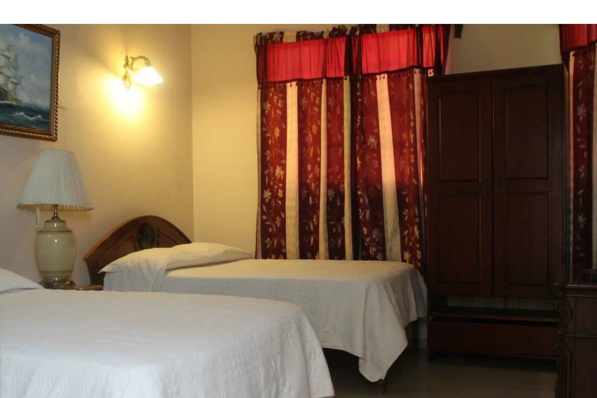 Habitación de hotel con dos camas individuales, una mesita de noche con lámpara, un armario de madera grande y un cuadro en la pared.
