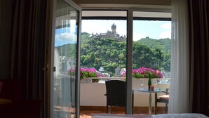 A hotel room with a large sliding glass door leading to a balcony with a view of a castle and lush greenery. - Flair Hotel Am Rosenhügel (Cochem)
