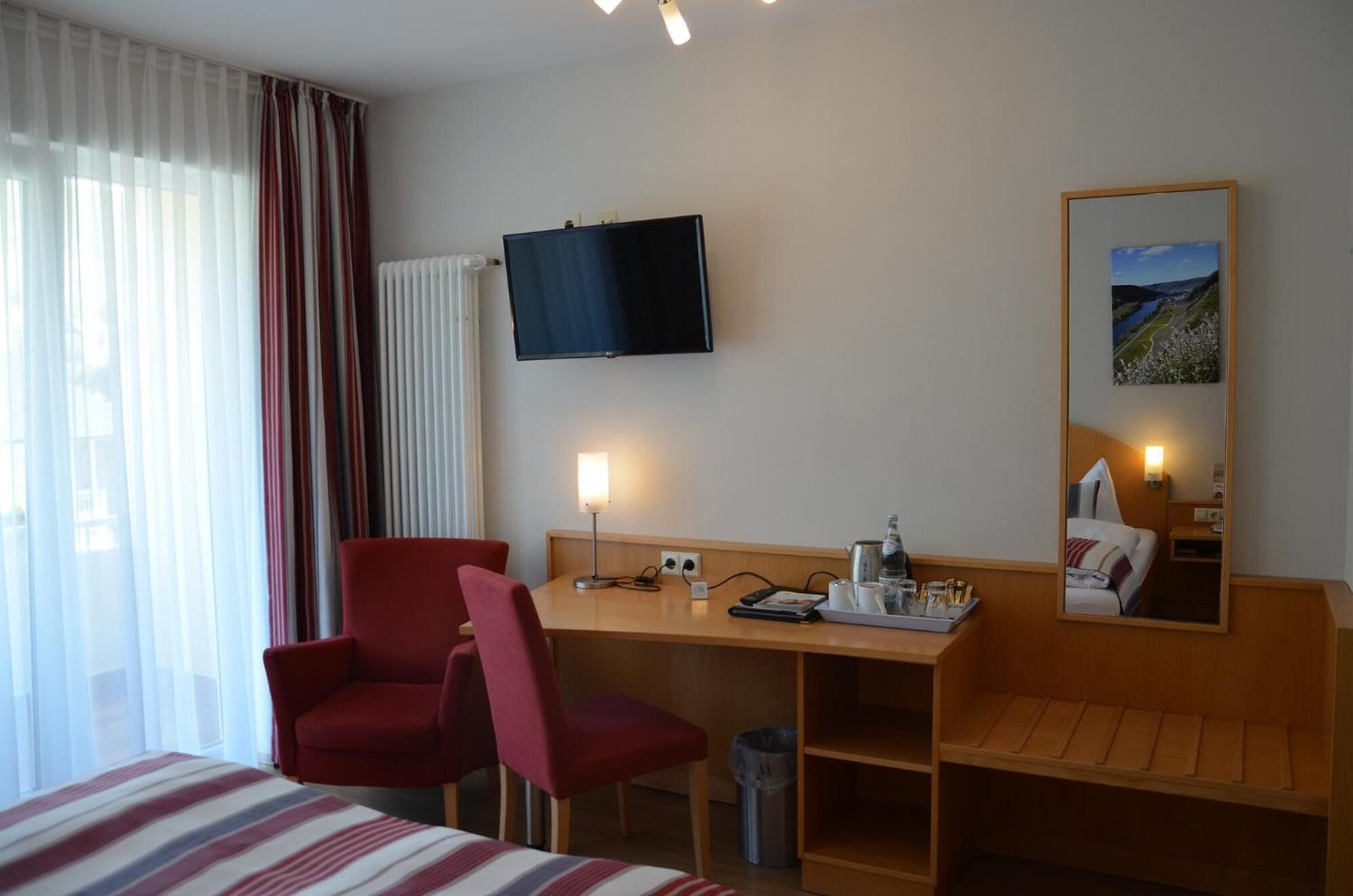 A hotel room with a bed, a desk, a chair, a TV, a mirror, and a window with curtains.
