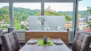 A dining area with a table set for two, a decorative vase, and a view of a castle on a hill. - Flair Hotel Am Rosenhügel (Cochem)