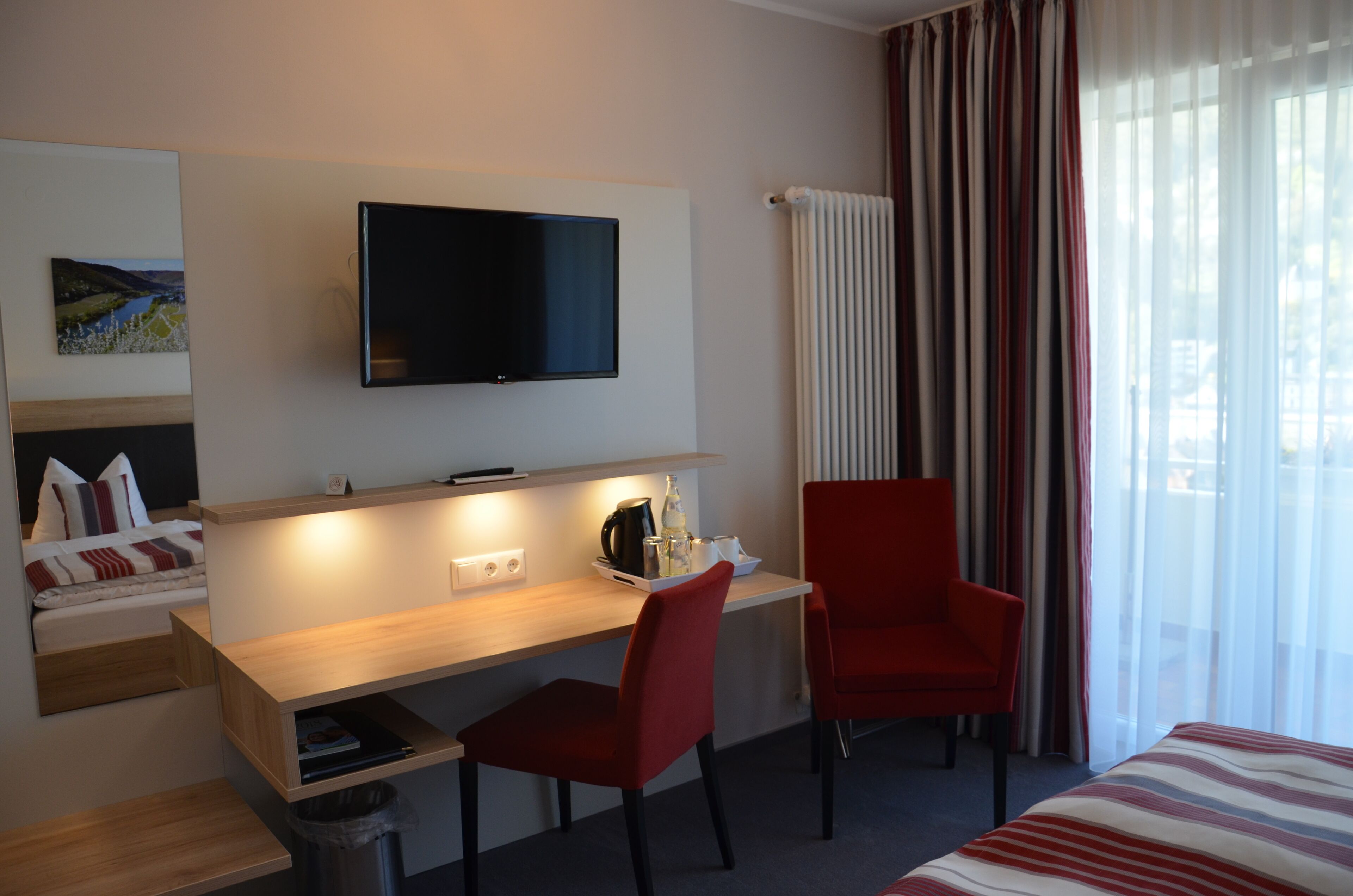 A hotel room with a bed, a desk with a chair, a TV, and a window with curtains.