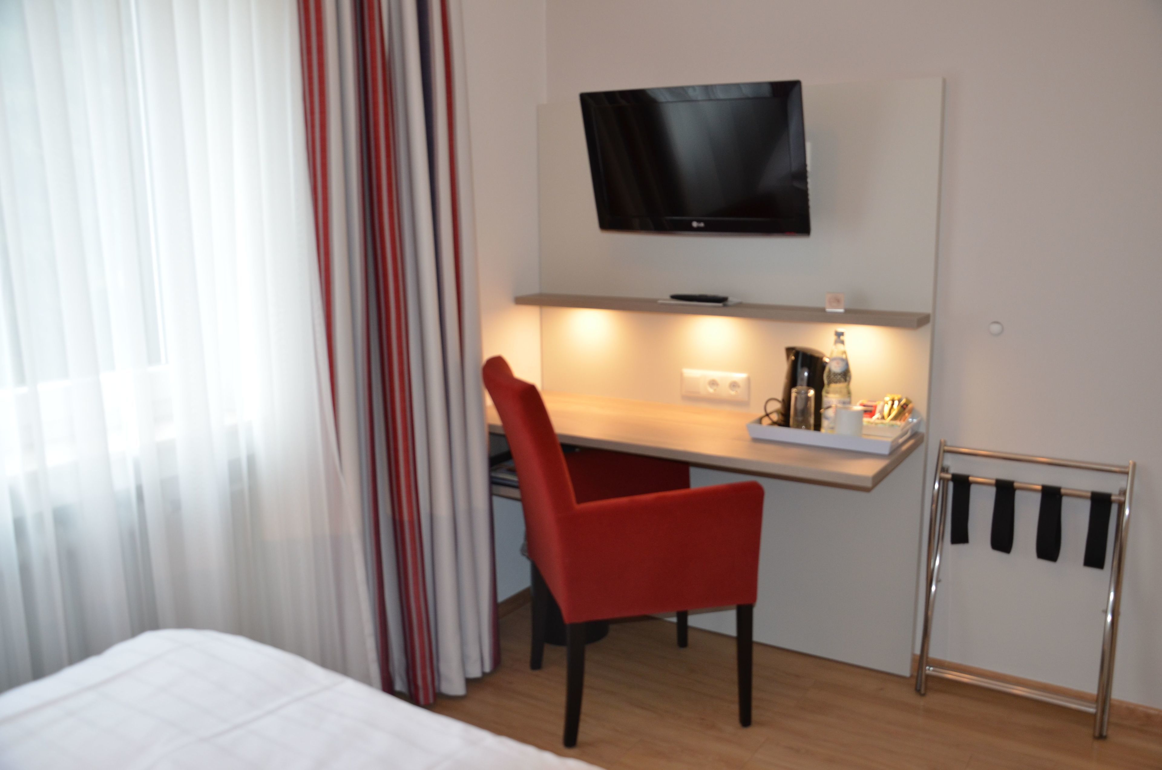 Hotelkamer met een bed, bureau met stoel, televisie boven het bureau en raam met gordijnen.