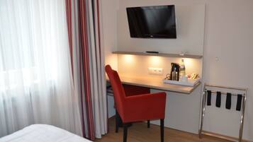 Hotelkamer met een bed, bureau met stoel, televisie boven het bureau en raam met gordijnen.