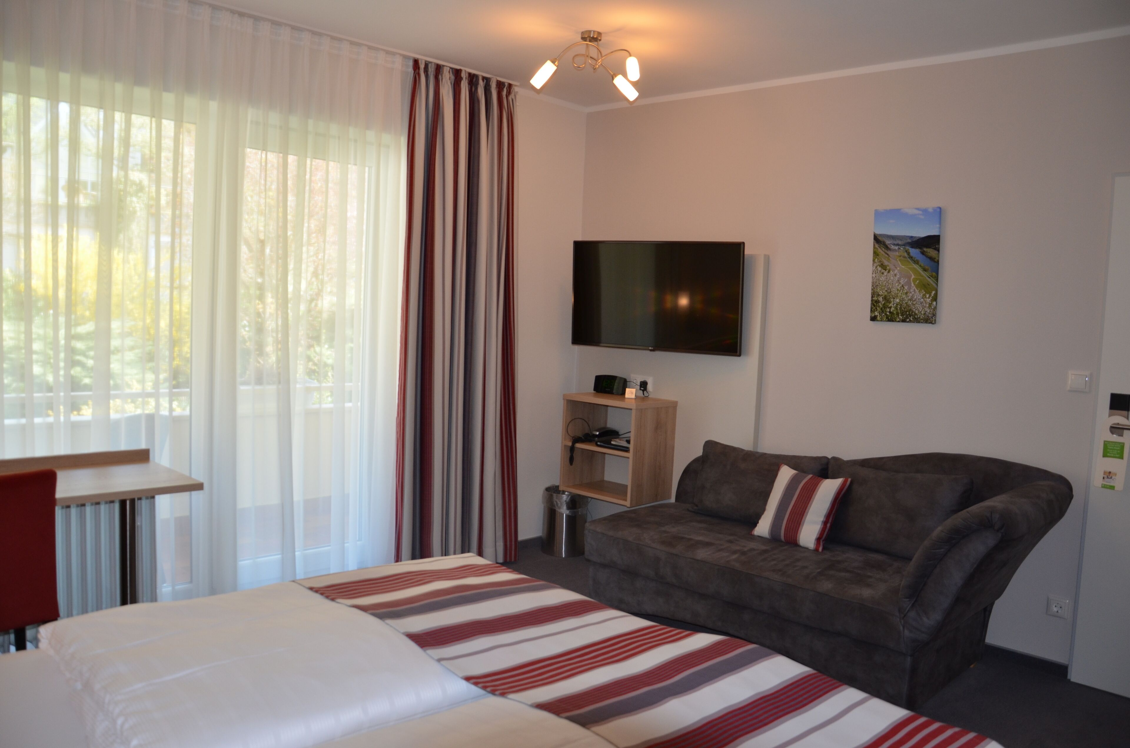 Ein Hotelzimmer mit Bett, Sofa, Fernseher, einem kleinen Tisch und einem Fenster mit Vorhängen.