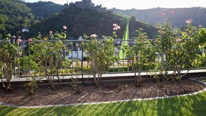 A garden with rose bushes and a castle in the background. - Flair Hotel Am Rosenhügel (Cochem)