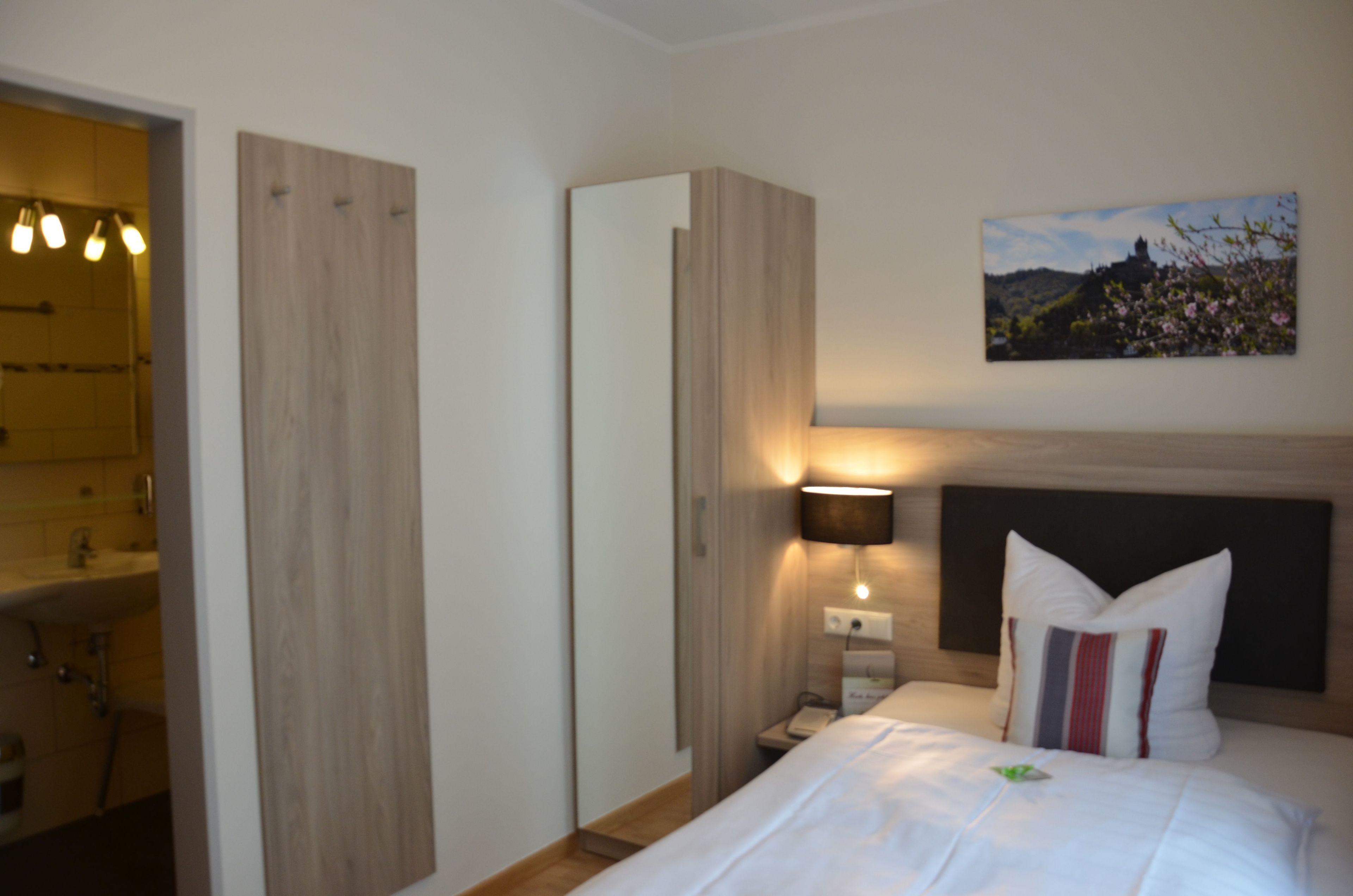 A hotel room with a bed, a bedside lamp, a painting on the wall, and a wooden wardrobe.