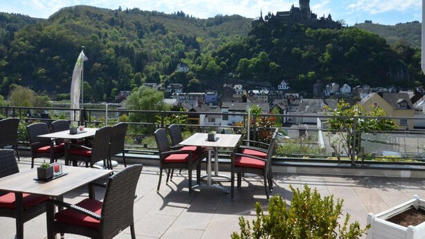 An outdoor patio with tables and chairs, overlooking a town and a castle on a hill. - Flair Hotel Am Rosenhügel (Cochem)