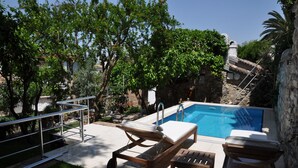Une piscine avec une terrasse en bois, des chaises longues et un mur en pierre.