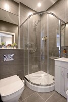 Un baño moderno con ducha de vidrio, inodoro blanco y tocador con espejo.