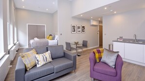 A modern living room with a grey sofa, a purple armchair, and a dining area with a small table and chairs.