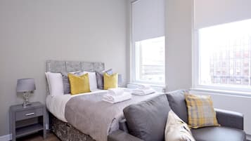 Une chambre à coucher moderne avec un lit, des tables de chevet, un canapé et une fenêtre.