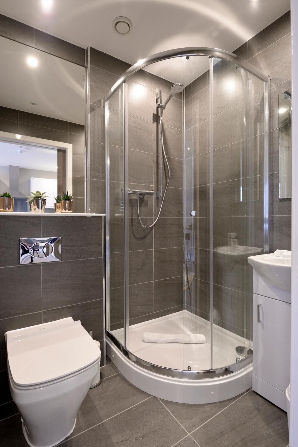 A modern bathroom with a glass-enclosed shower, a toilet, and a sink.
