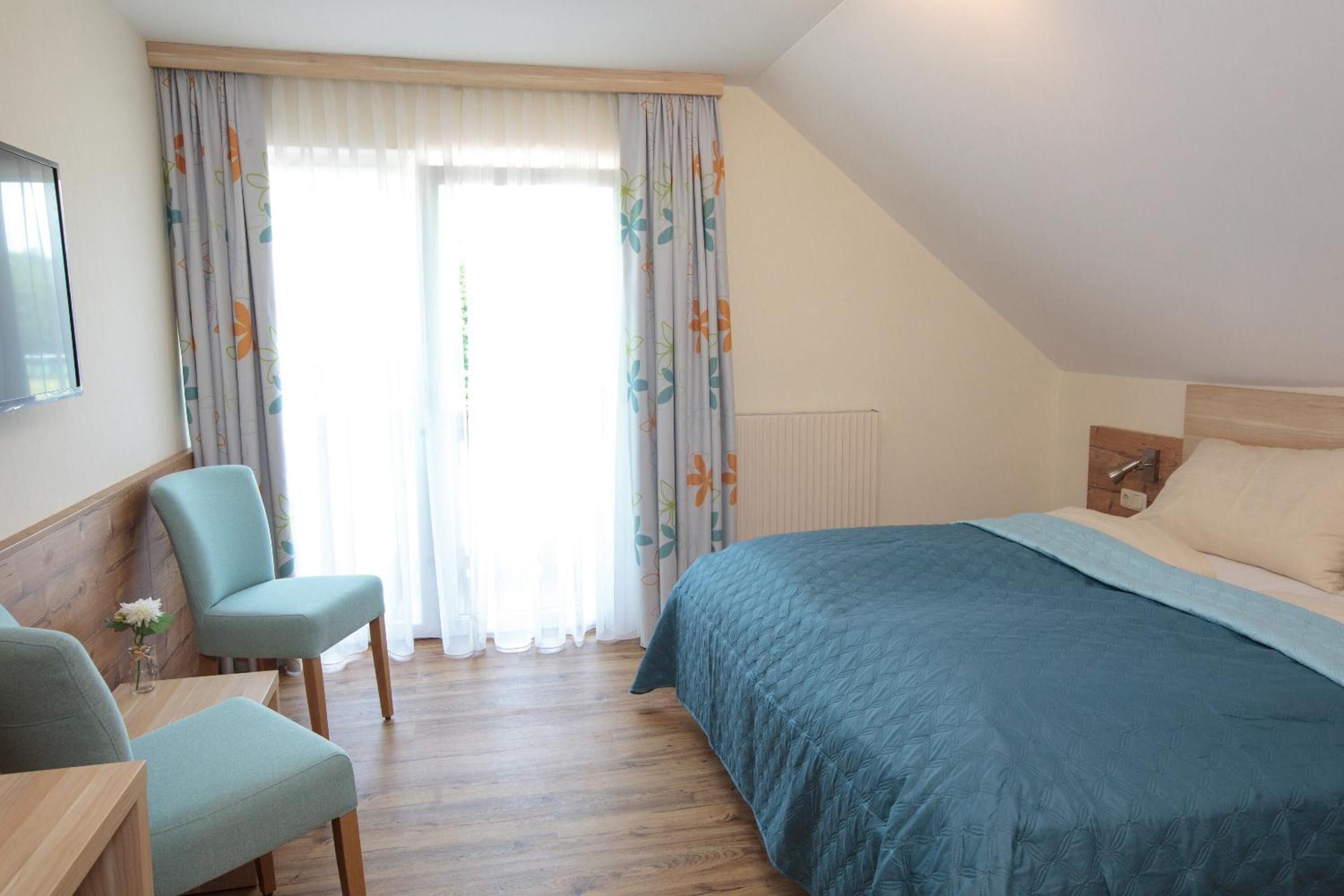 A bedroom with a bed, a chair, a table, and a window with curtains.
