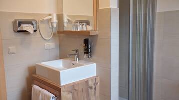 A bathroom with a white sink, a wooden cabinet, a towel hanging on the cabinet, a mirror above the sink, and a shower area with glass doors.