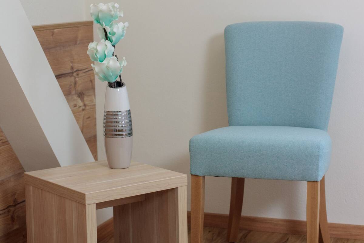 Een lichtblauwe fauteuil naast een klein houten tafeltje met een bloemenvaas.