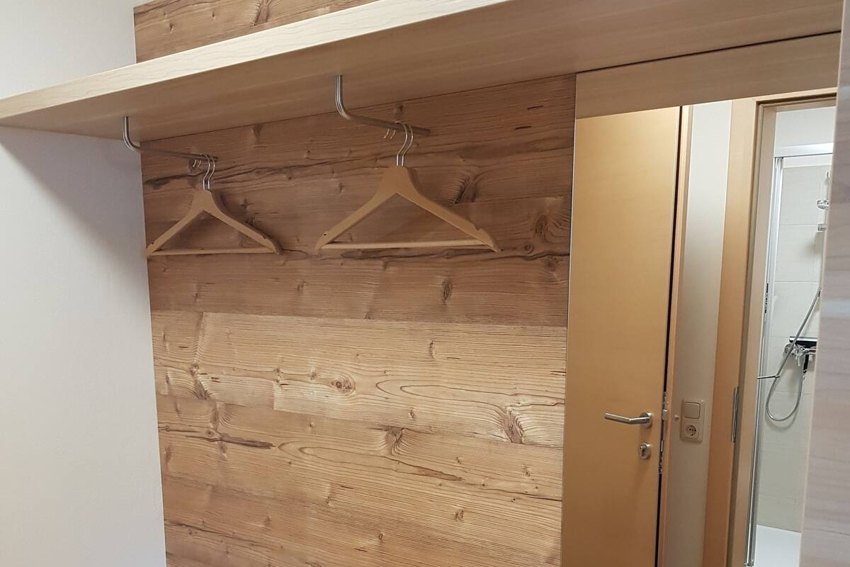 Een houten garderobe met spiegel, kledingrek en een bankje.