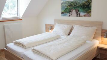 A bedroom with a wooden bed, white bedding, a window, a radiator, and a painting of a lake.