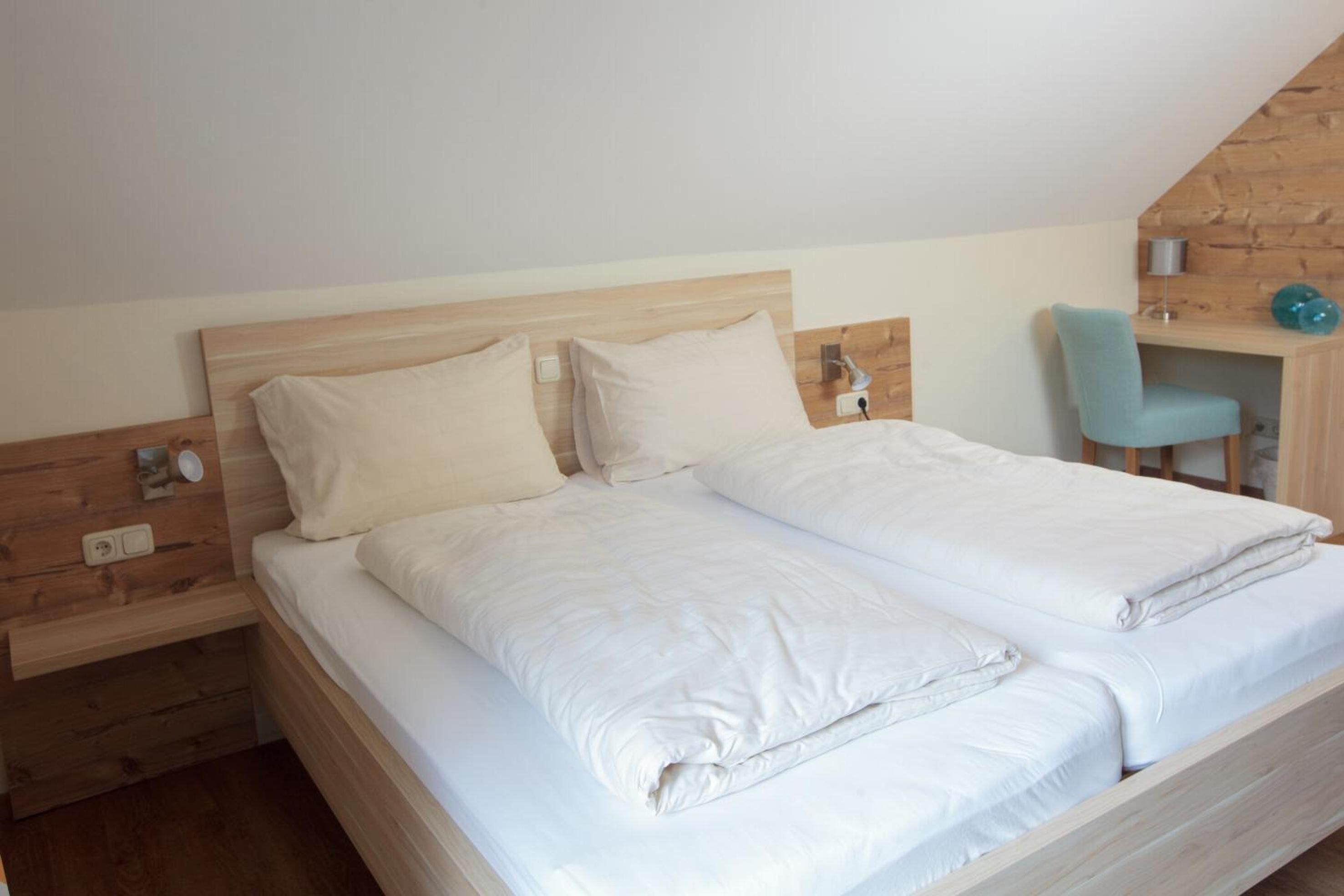 Ein Doppelbett mit weißer Bettwäsche in einem Raum mit Holzwänden und einer geneigten Decke.