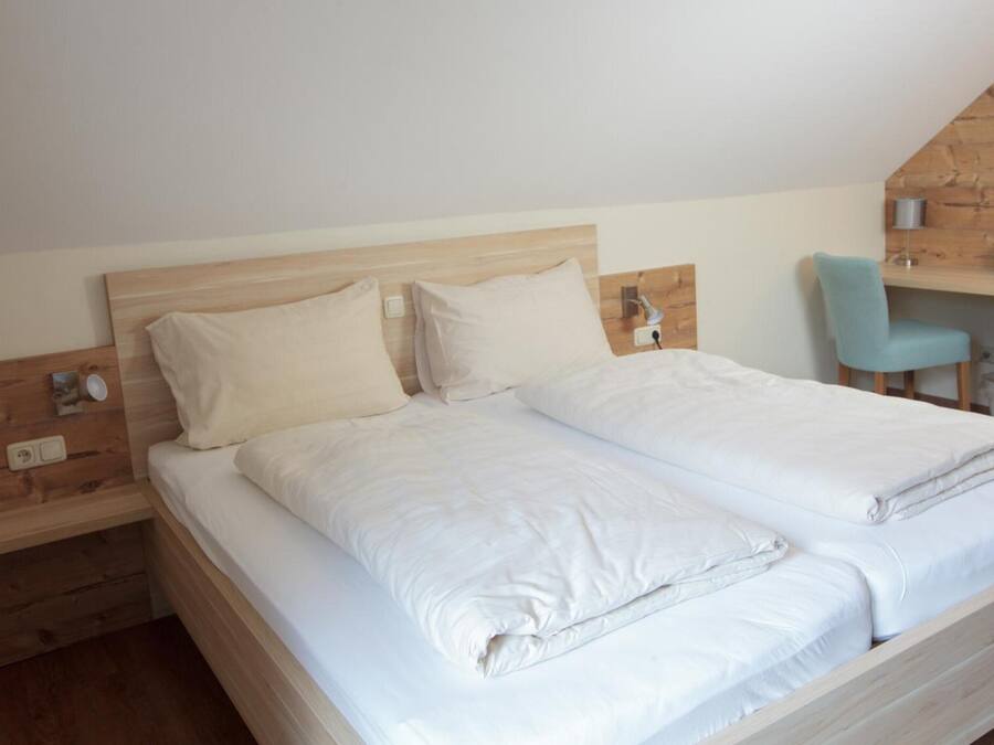 Ein Doppelbett mit weißer Bettwäsche in einem Raum mit Holzwänden und einer geneigten Decke.