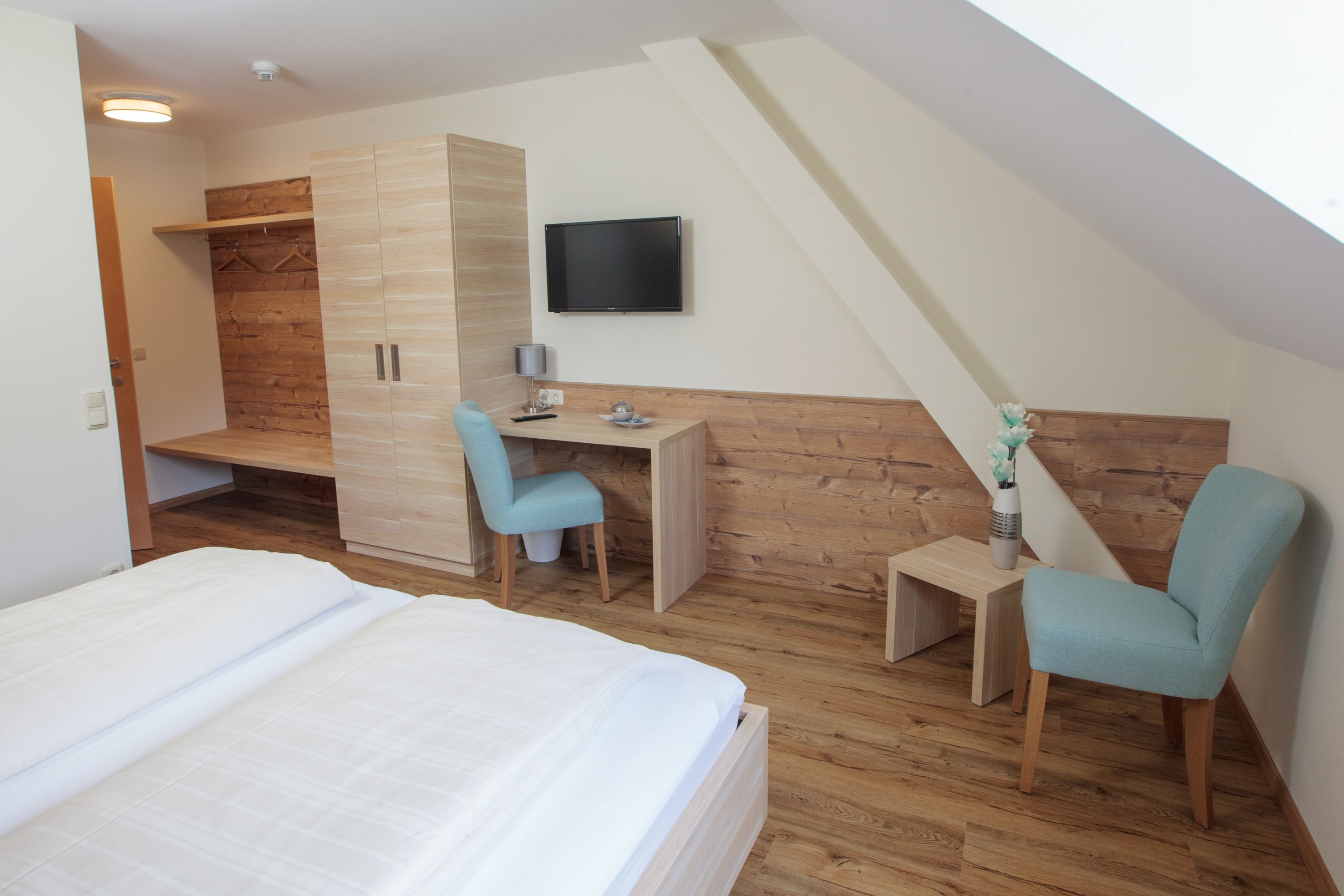 Ein Schlafzimmer mit einem Bett, einem Schreibtisch, zwei Stühlen, einem Fernseher und einem Kleiderschrank.