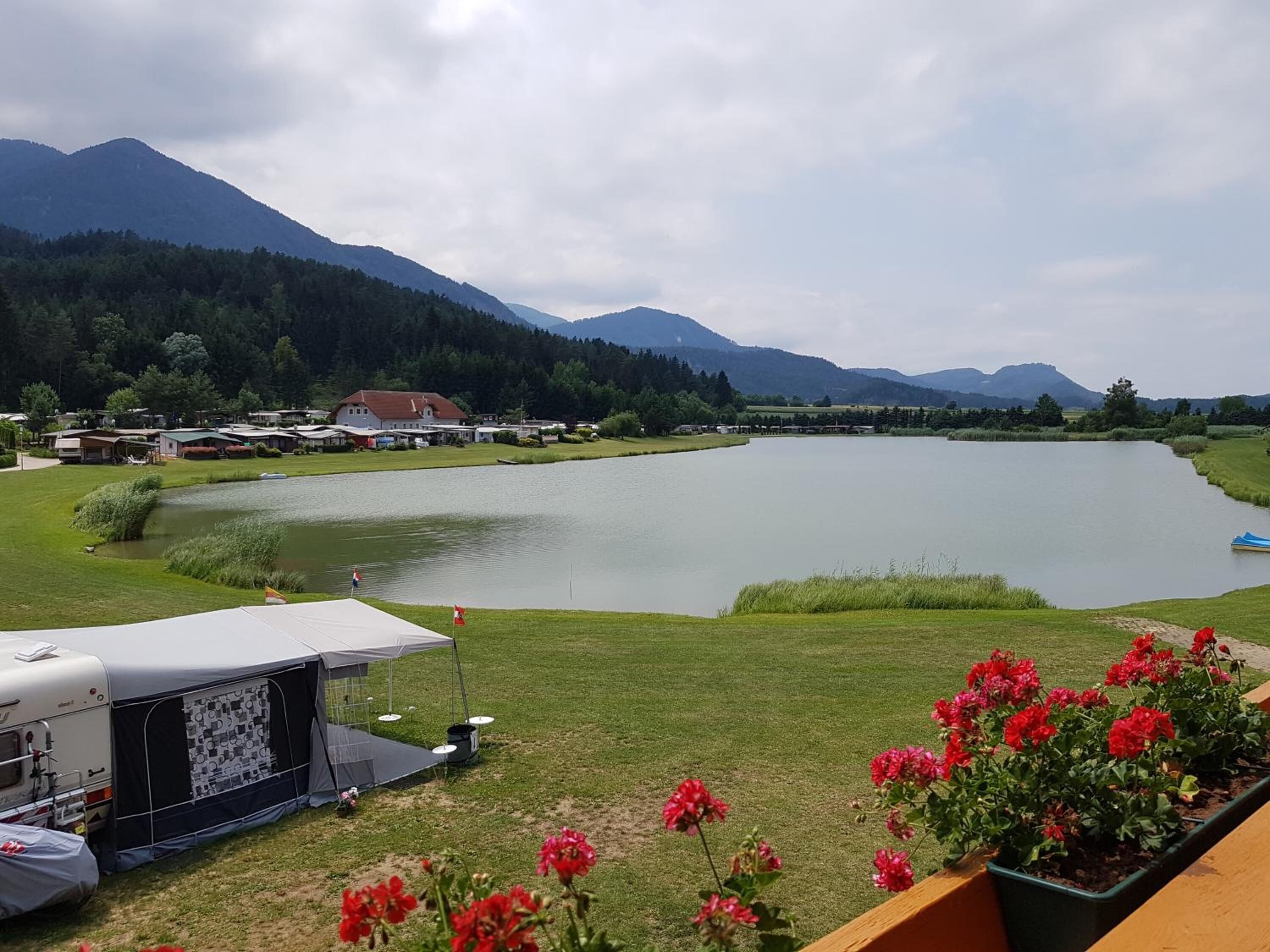 A lakeside view with a camping area, a trailer, and a flower bed.