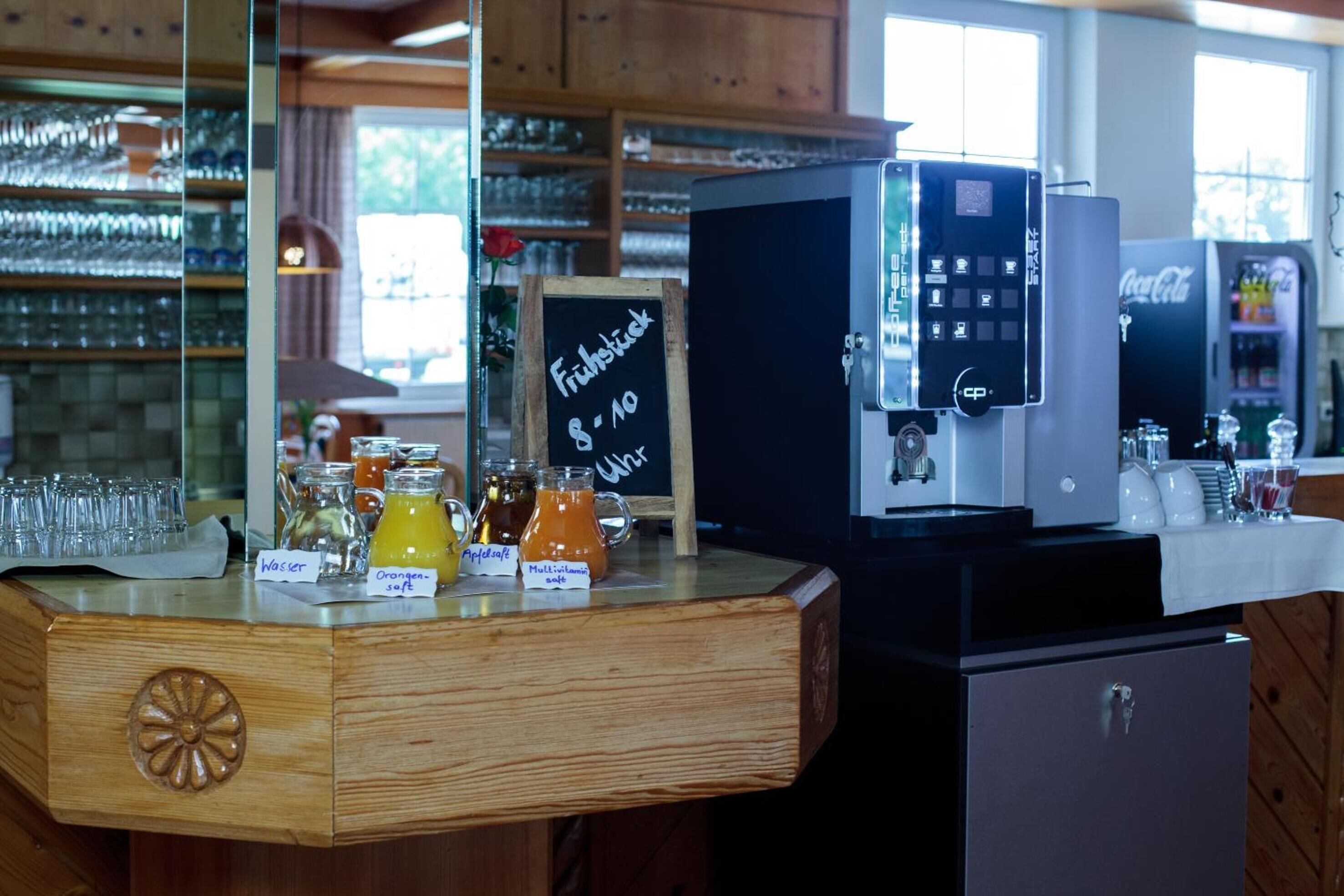 Zona de bar con una máquina de café, un menú en la pizarra y varios dispensadores de bebidas.