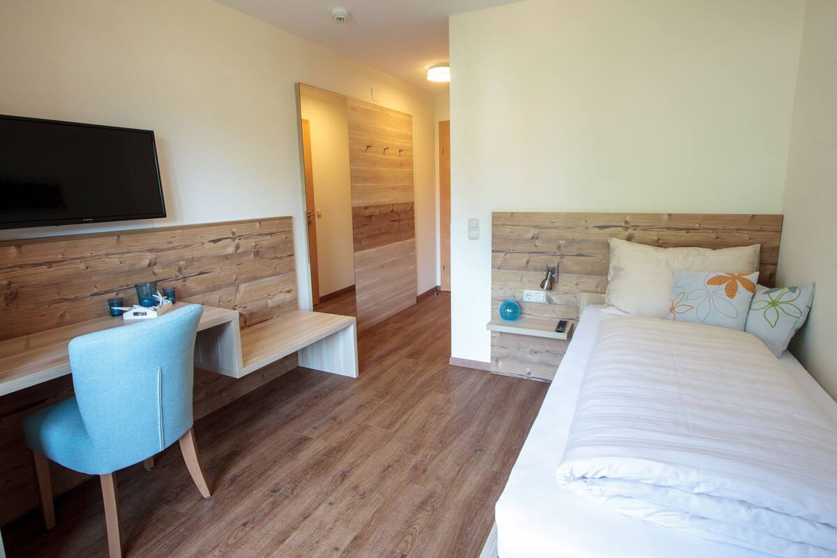 Een hotelkamer met een bed, bureau, stoel, televisie en een houten wandpaneel.
