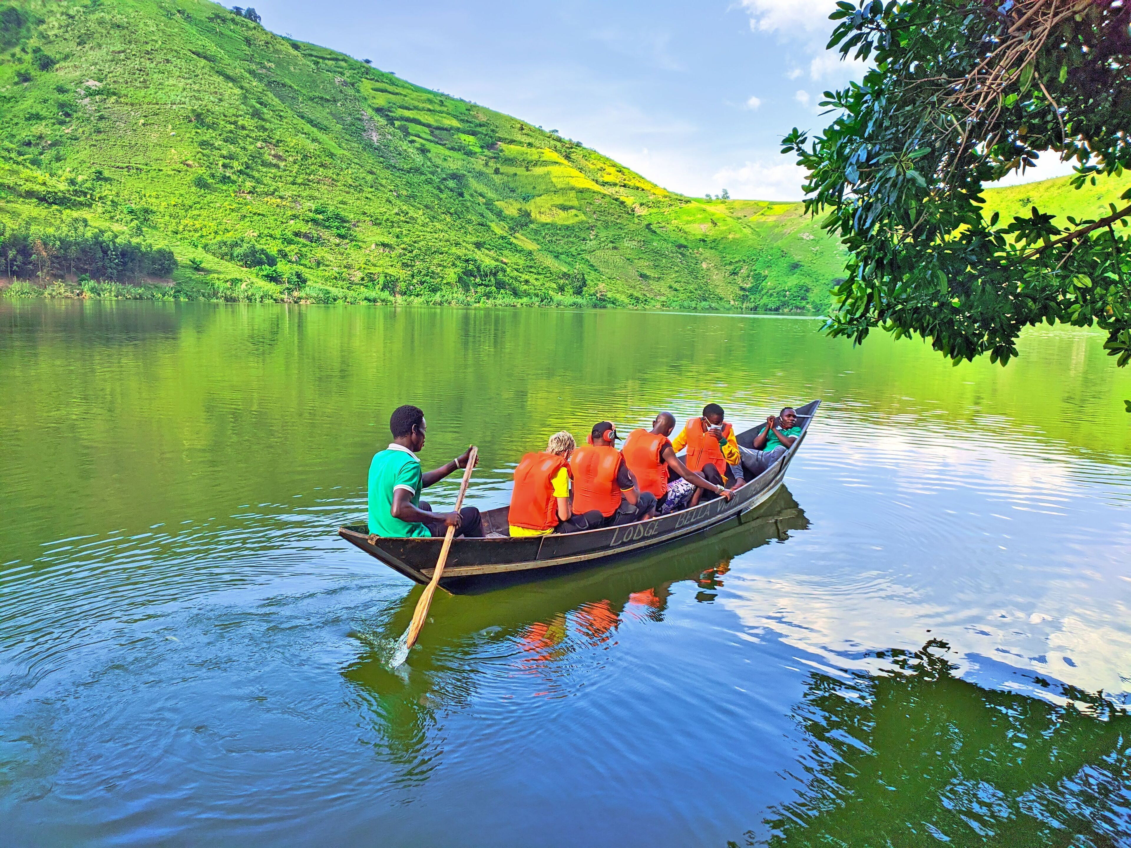 A rowboat with passengers wearing life jackets on a calm lake surrounded by lush greenery.