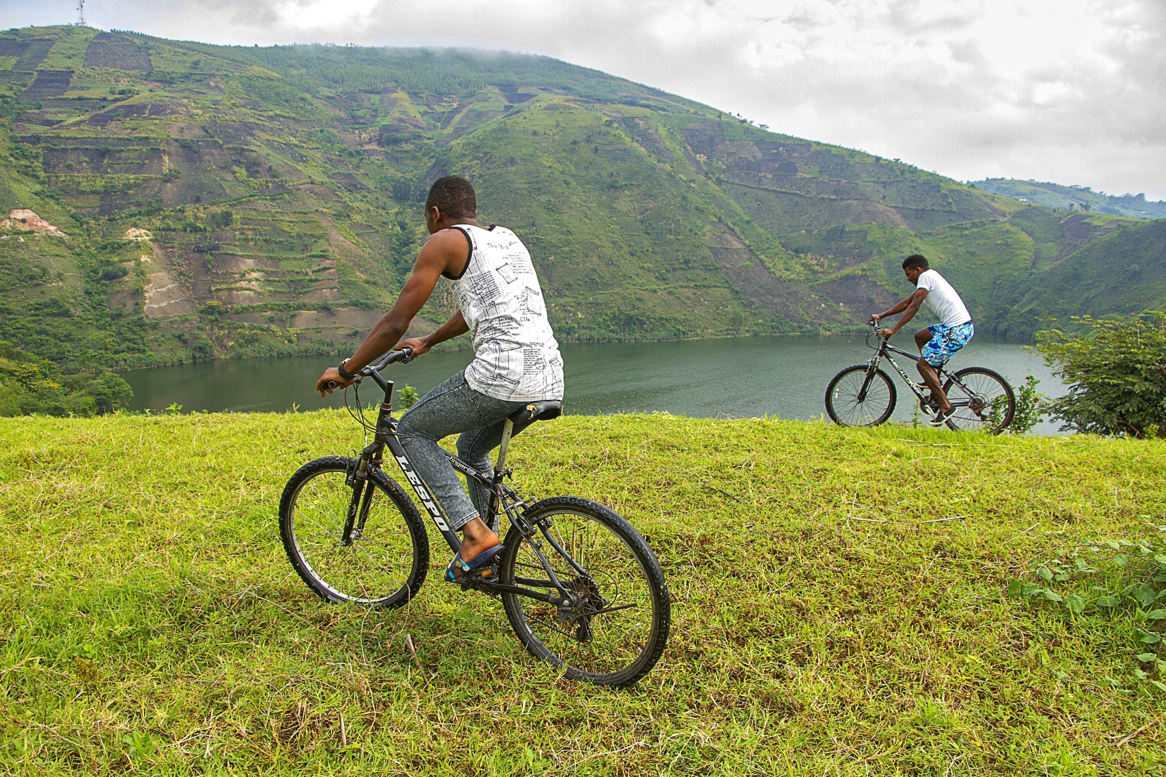 Due ciclisti su una collina erbosa con vista su un lago e montagne sullo sfondo.