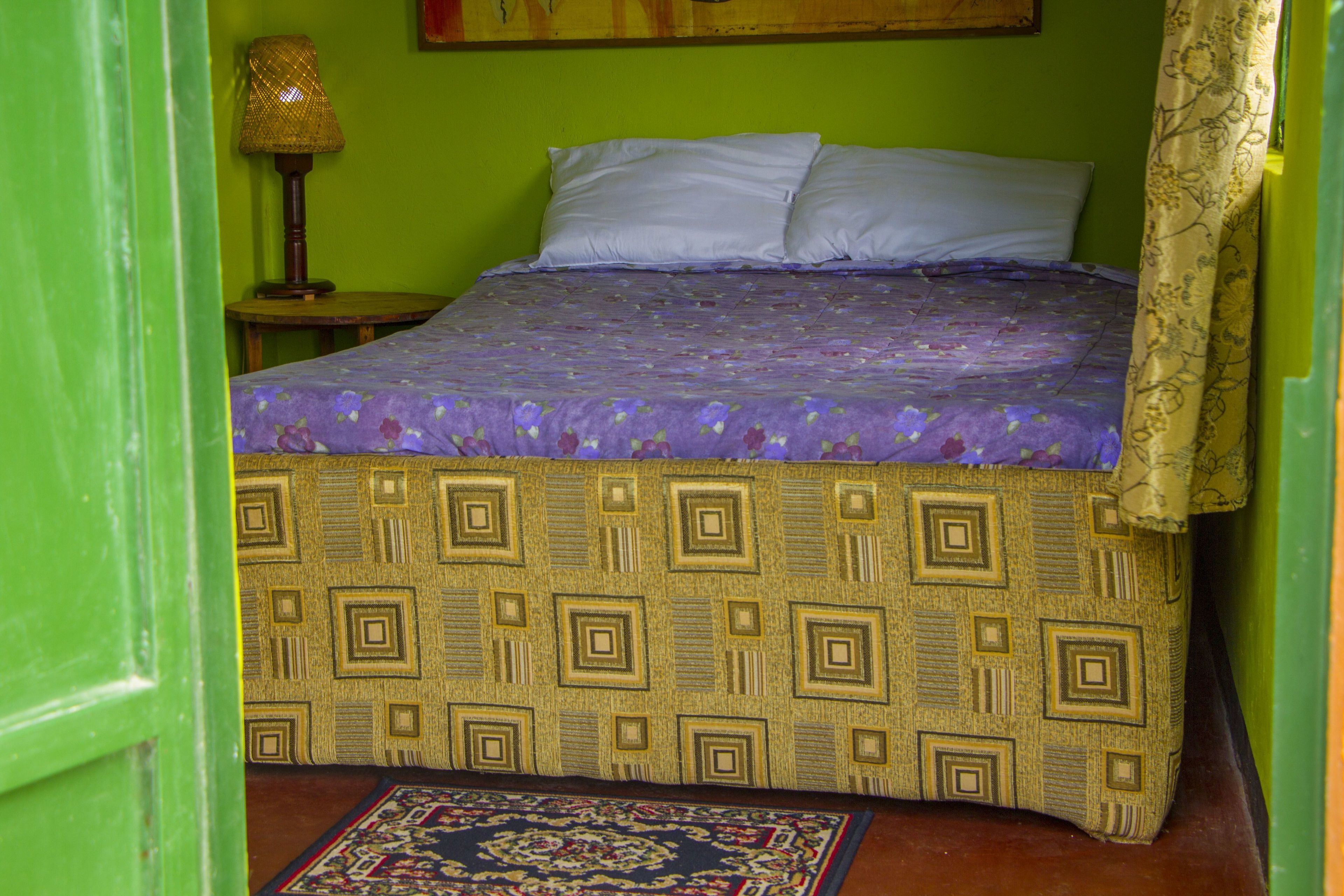 Una cama con una colcha estampada, una mesita de noche con una lámpara y una alfombra decorativa en el suelo.