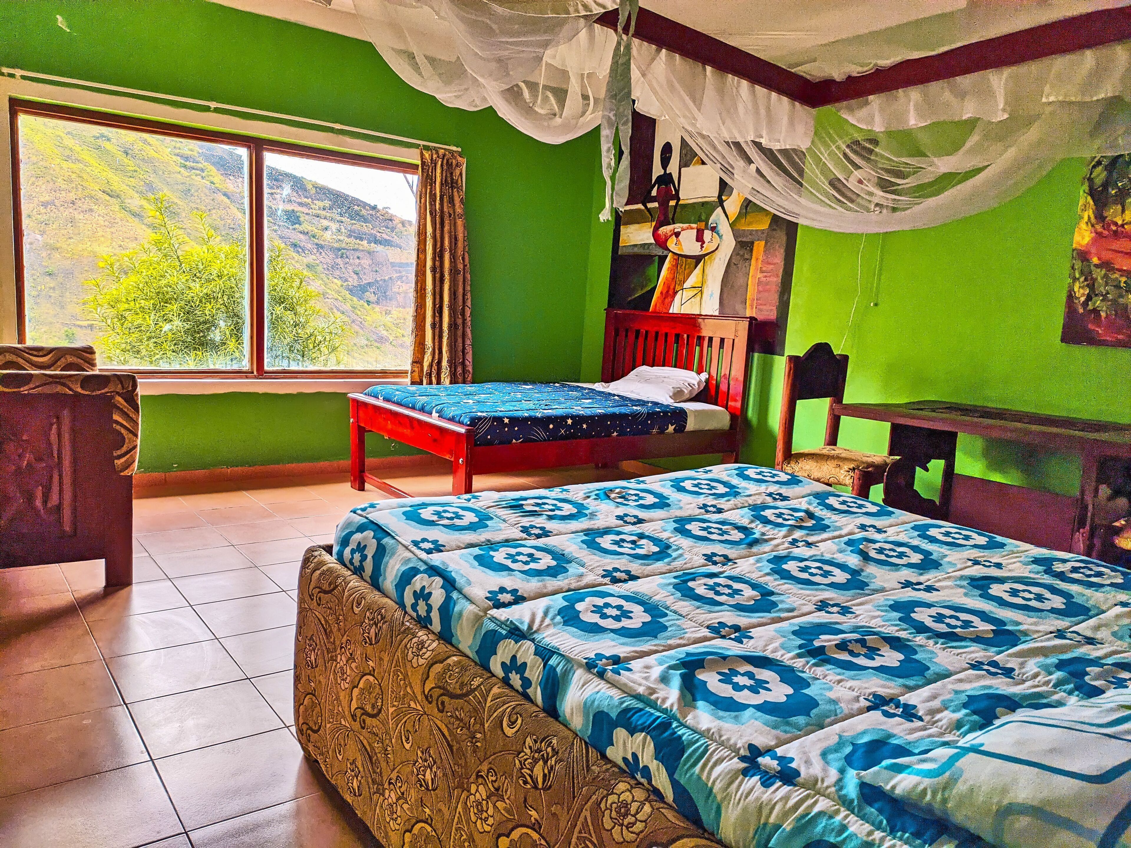 A room with a bed, a chair, a small table, and a window with a view of hills.