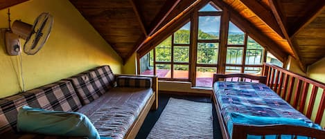 Quarto de sótão aconchegante com duas camas de madeira, um sofá e uma janela grande com vista para um lago.