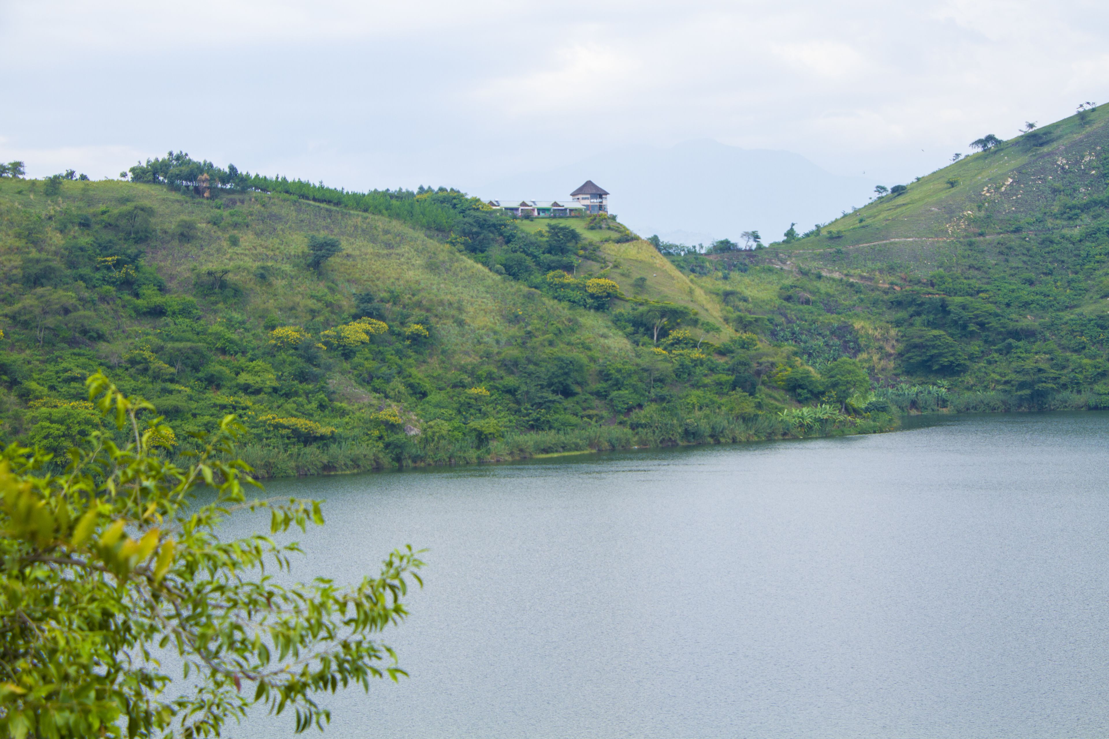 Un lac paisible, entouré de collines verdoyantes, avec un petit bâtiment perché au sommet d’une de ces collines.