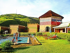 Un edificio con aspecto de castillo, con piscina, rodeado de céspedes cuidados y bancos rojos.