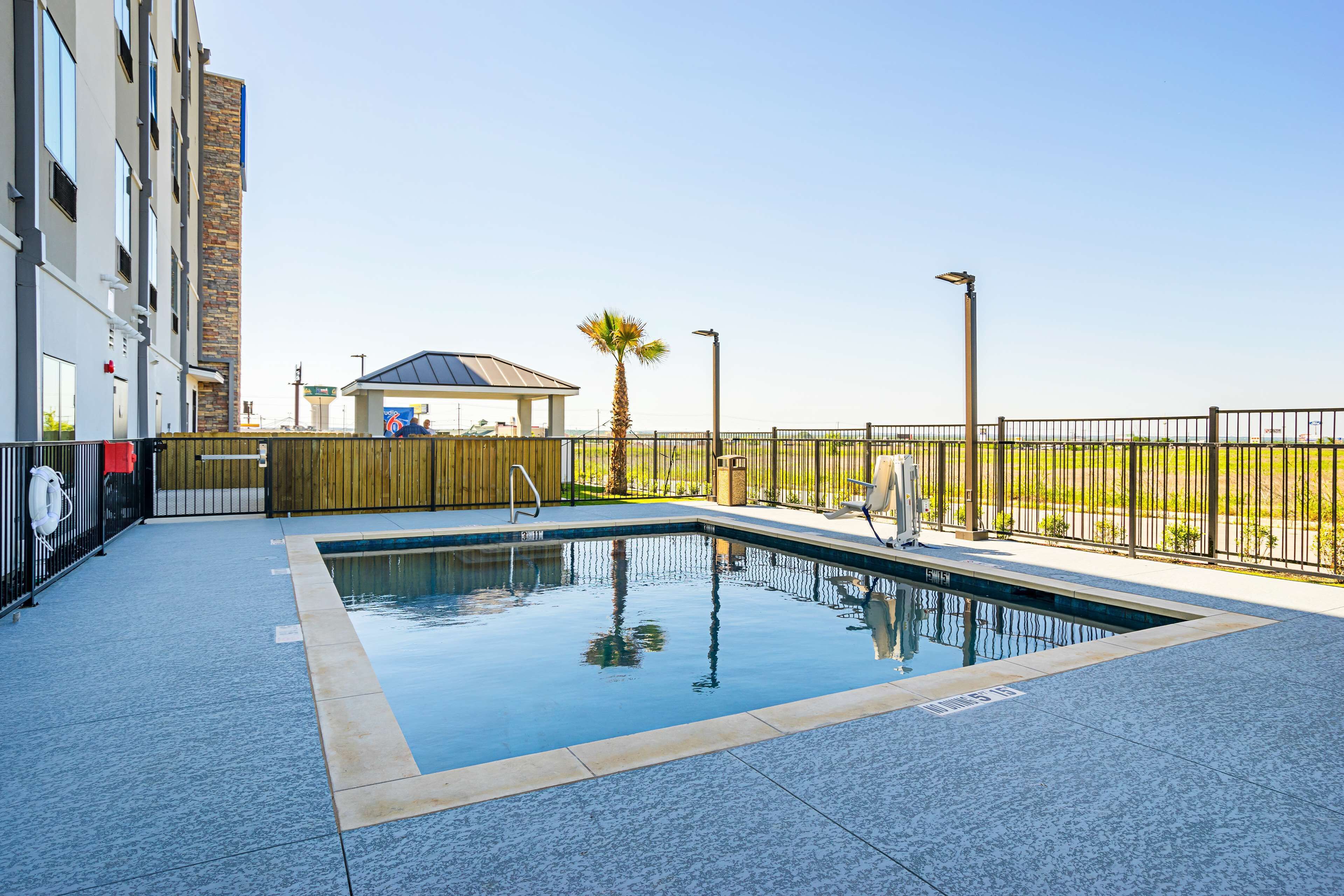 Une piscine avec une terrasse carrelée, une clôture en bois et un bâtiment en arrière-plan.