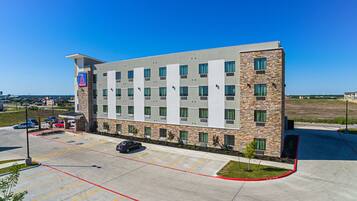 A modern hotel with a stone facade, multiple floors, and a parking lot with marked spaces.