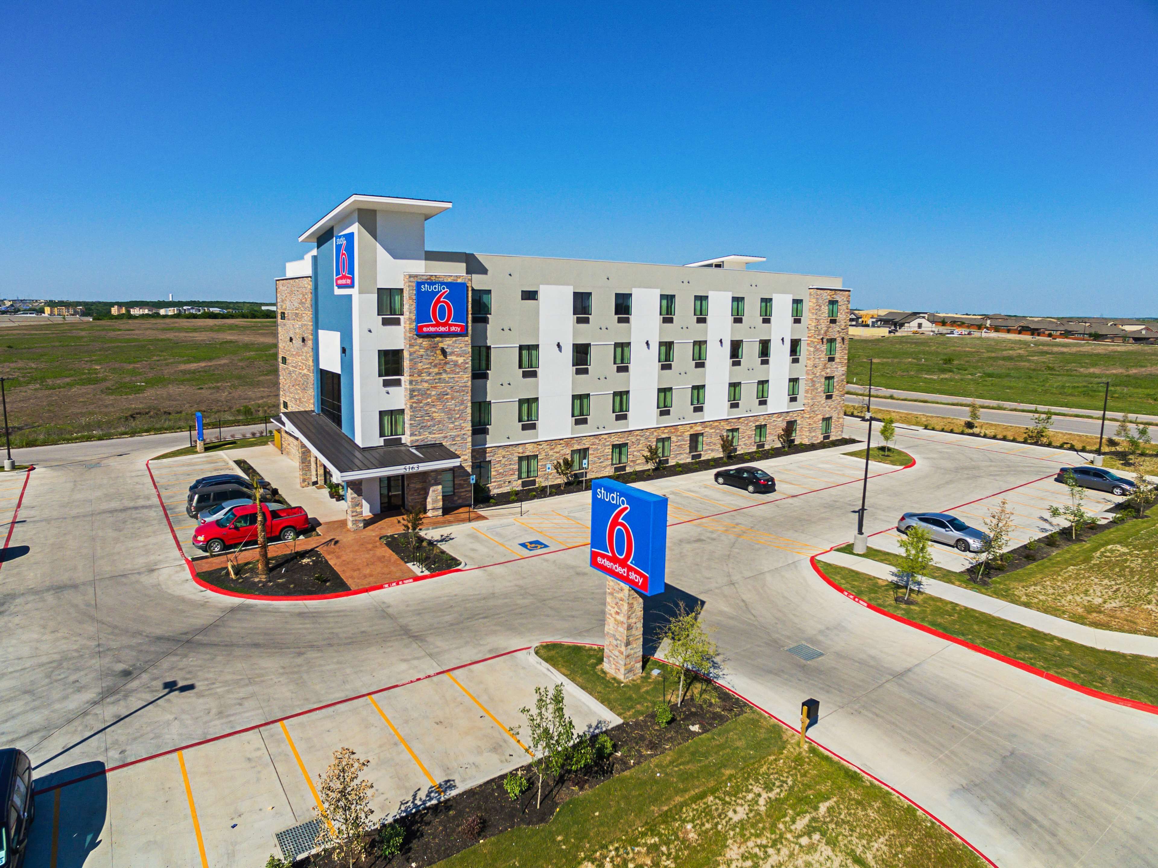 A multi-story hotel with a modern design, featuring a parking lot with marked spaces, a central entrance, and a prominent signage indicating extended stay availability.