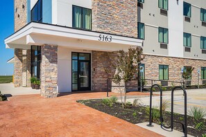 A modern building with a stone facade, numbered 5163, featuring a covered entrance and a parking area with a metal bike rack. - Studio 6 Buda, TX (Buda)