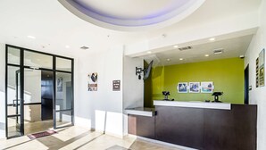 A reception area with a green wall, a reception desk, and a glass door entrance. - Studio 6 Buda, TX (Buda)