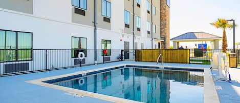 A rectangular outdoor pool with a clear blue water surface, surrounded by a low black metal fence.