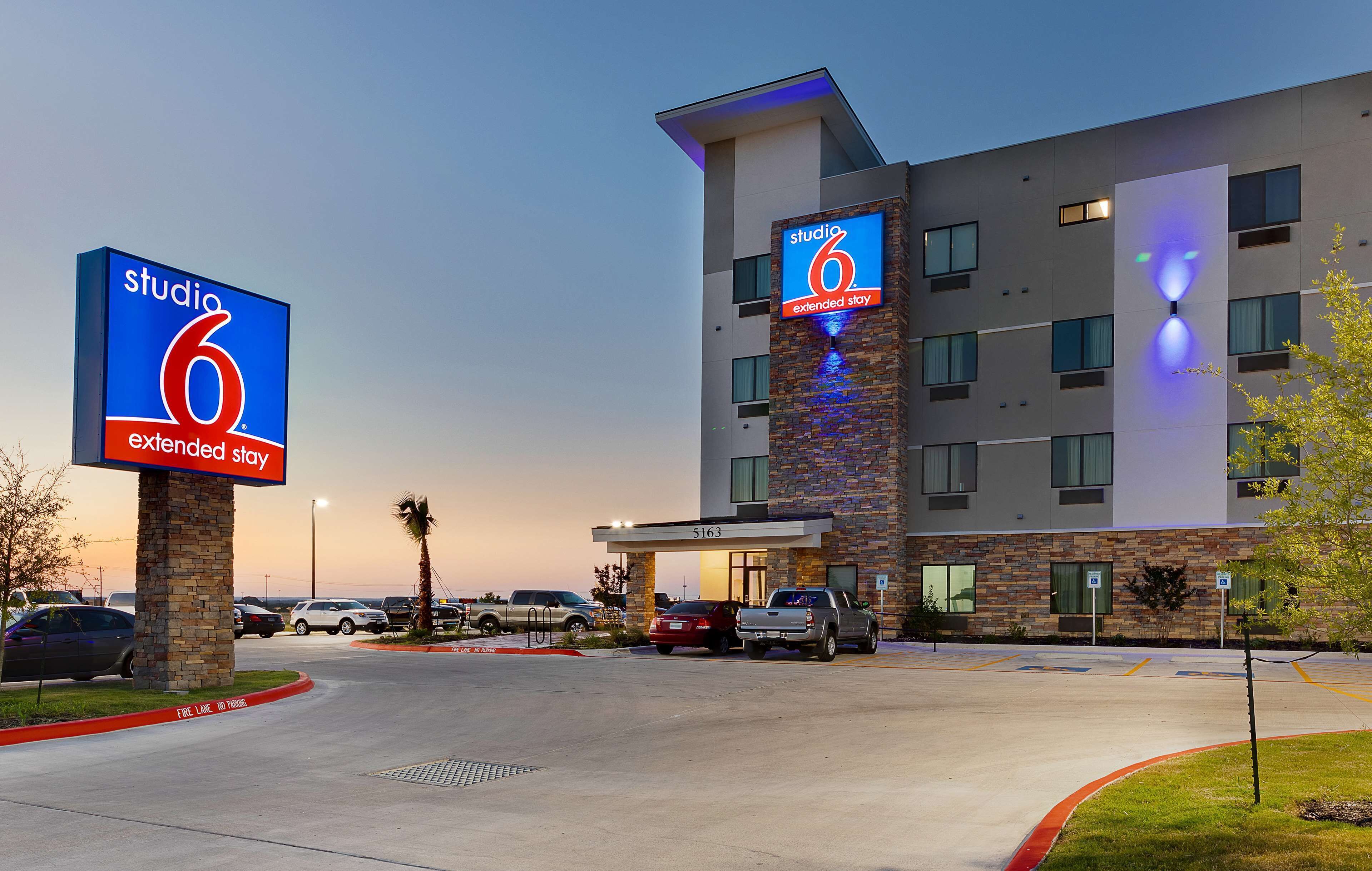 A modern hotel with a prominent 'Studio 6 Extended Stay' sign, a parking lot, and a building with multiple windows and a brick facade.
