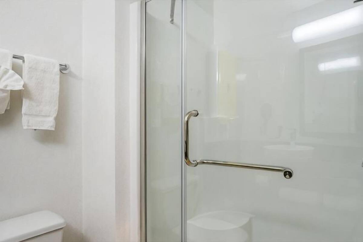 Puerta de ducha de vidrio con un tirador metálico, un inodoro blanco y un perchero con dos toallas.